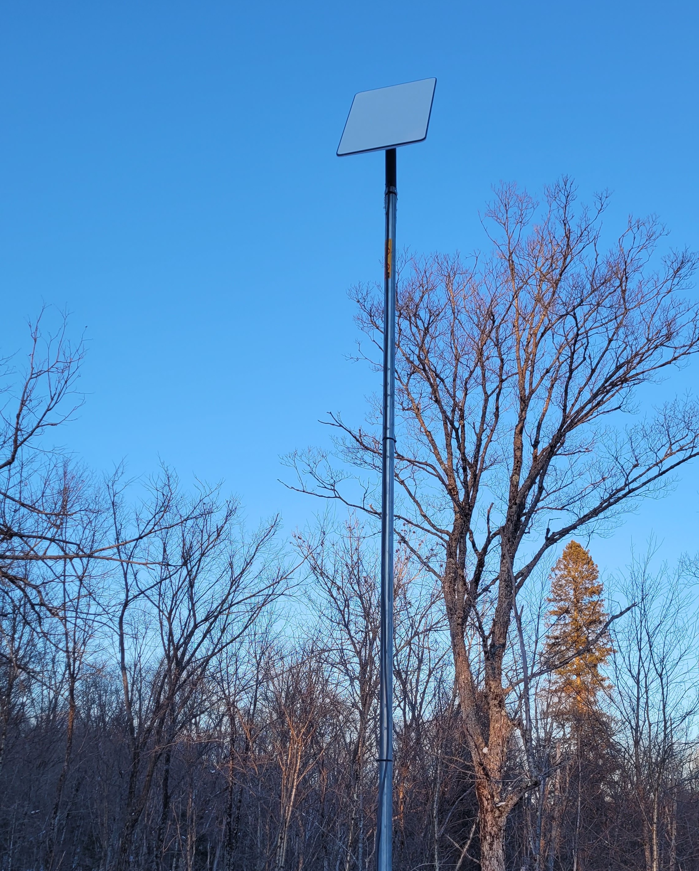 starlink dish with a 10-foot rod installed on a roof with trees in the background