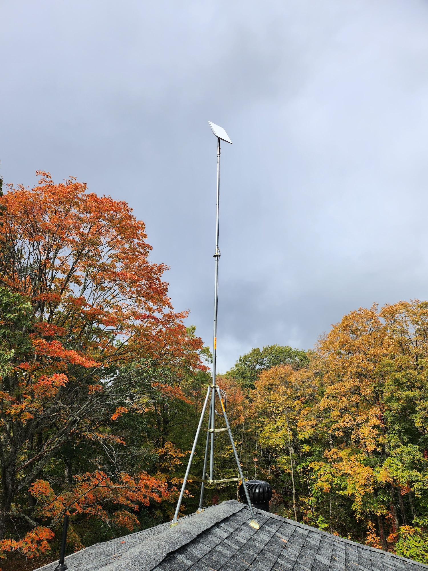 15 foot starlink tower on a rooftop tripod reaching above fall foliage